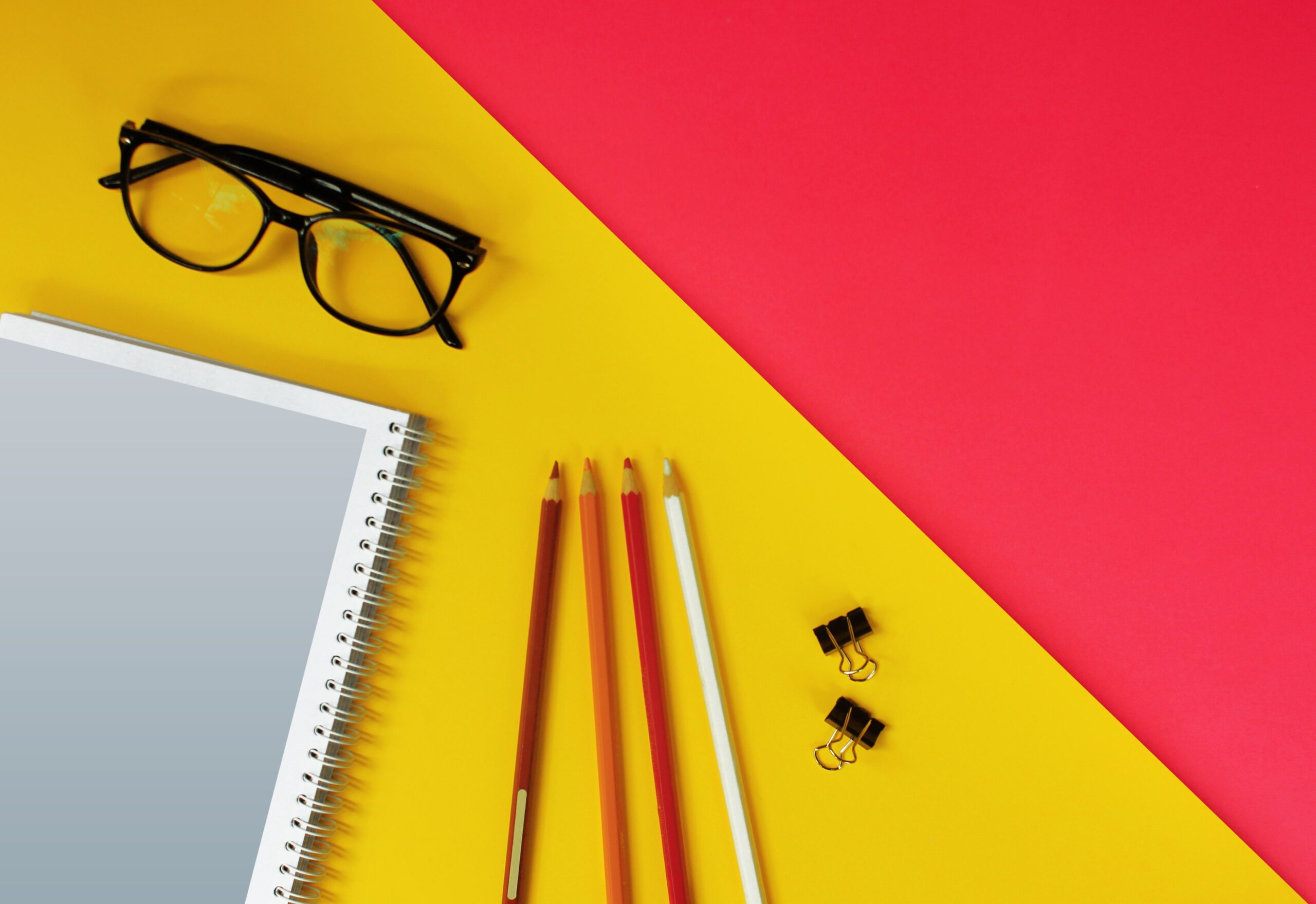 Quaderno, matite colorate e occhiali su sfondo giallo e rosso — strumenti di organizzazione personale e professionale